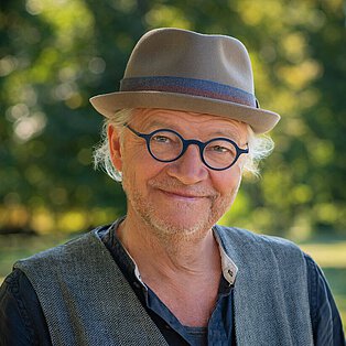 Bild von Dr. med. Michael Druse, Mann mit runder Brille, Hut auf dem Kopf, lächelt